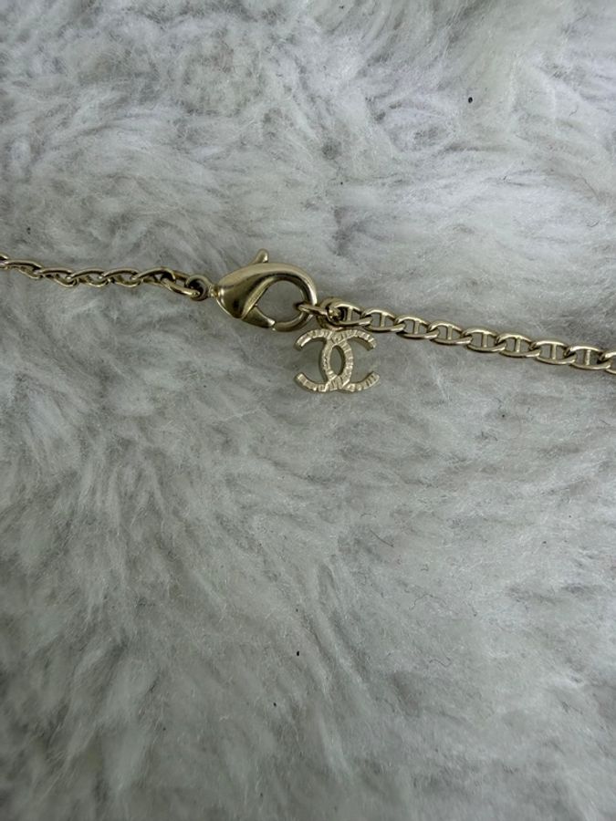 這條 Chanel 品牌項鍊以金屬色細鍊搭配由紫色寶石與經典雙 C Logo 組成的花卉狀墜飾。-2