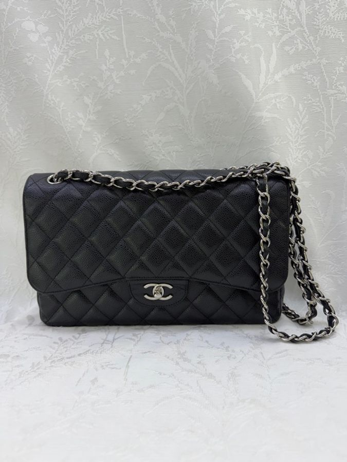 這是一只經典的黑色 CHANEL Classic Flap Jumbo 包款，採用耐用的魚子醬牛皮製成，並搭配銀色金屬鏈帶。-0